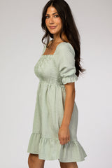 woman wearing a sage green and white gingham smocked maternity dress with puff sleeves