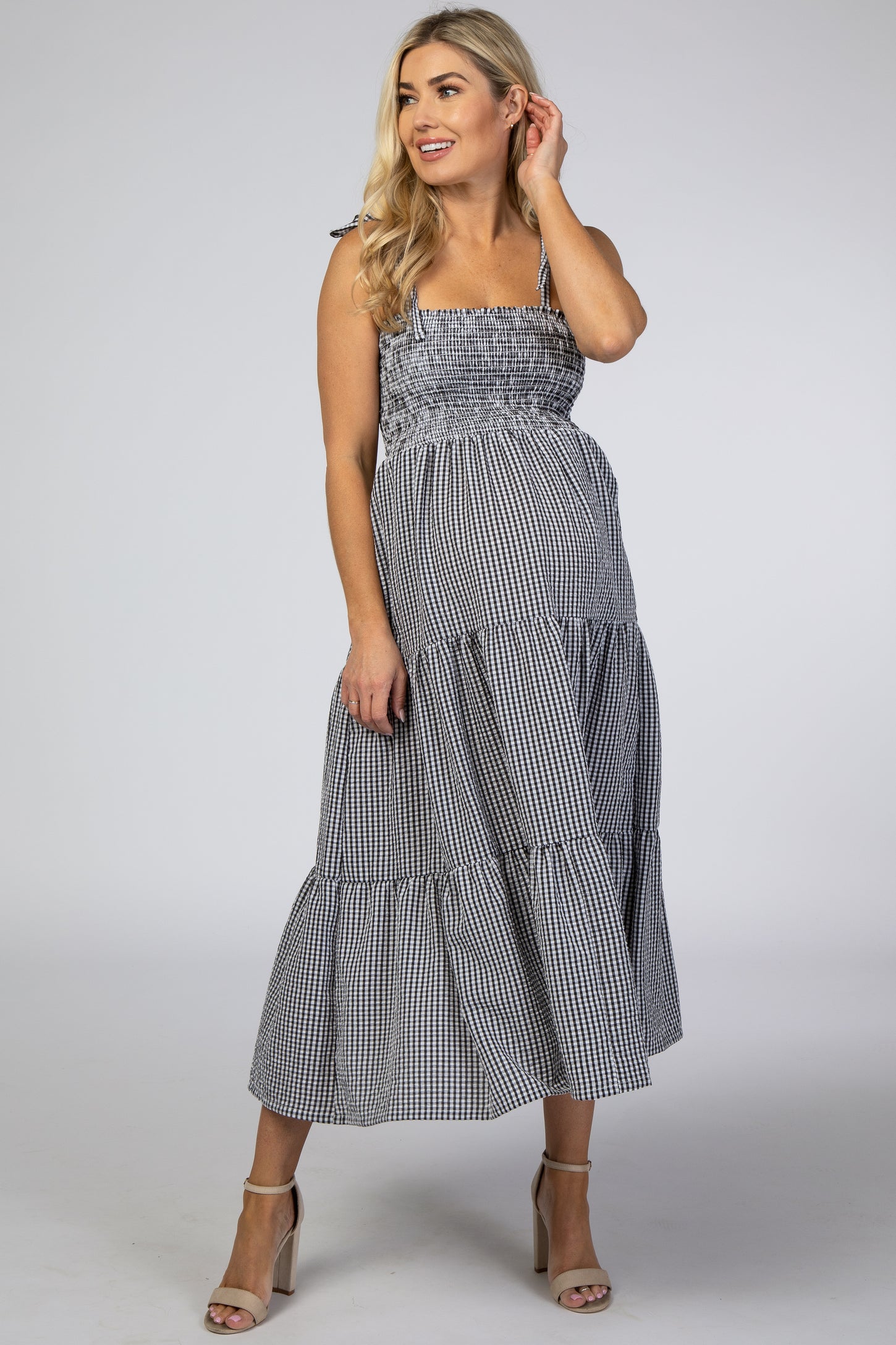 Pregnant woman wearing a black and white gingham smocked maternity midi dress with tiered skirt and heels