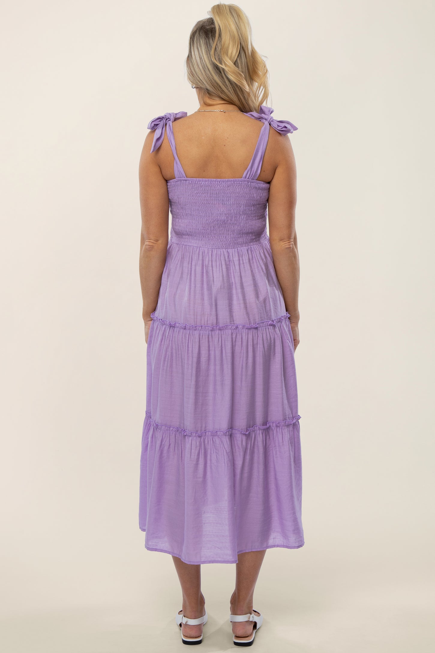 Back view of a woman wearing a lavender tiered midi dress with tie-shoulder straps and a smocked bodice