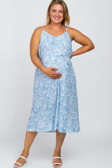 Smiling pregnant woman wearing a blue floral maternity midi dress with spaghetti straps and a waist tie.