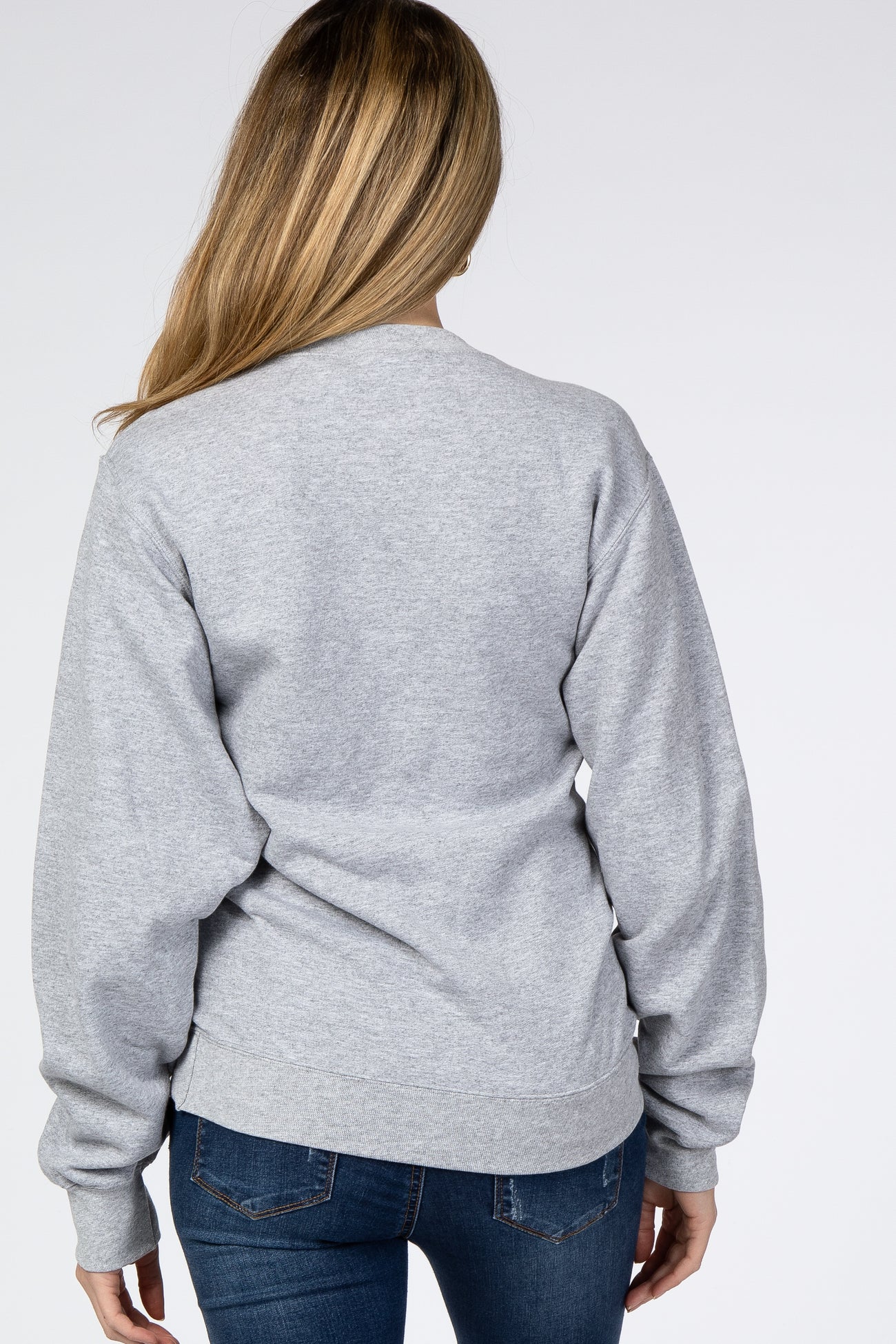 Back view of a woman wearing a grey crew neck sweatshirt and blue jeans against a white background