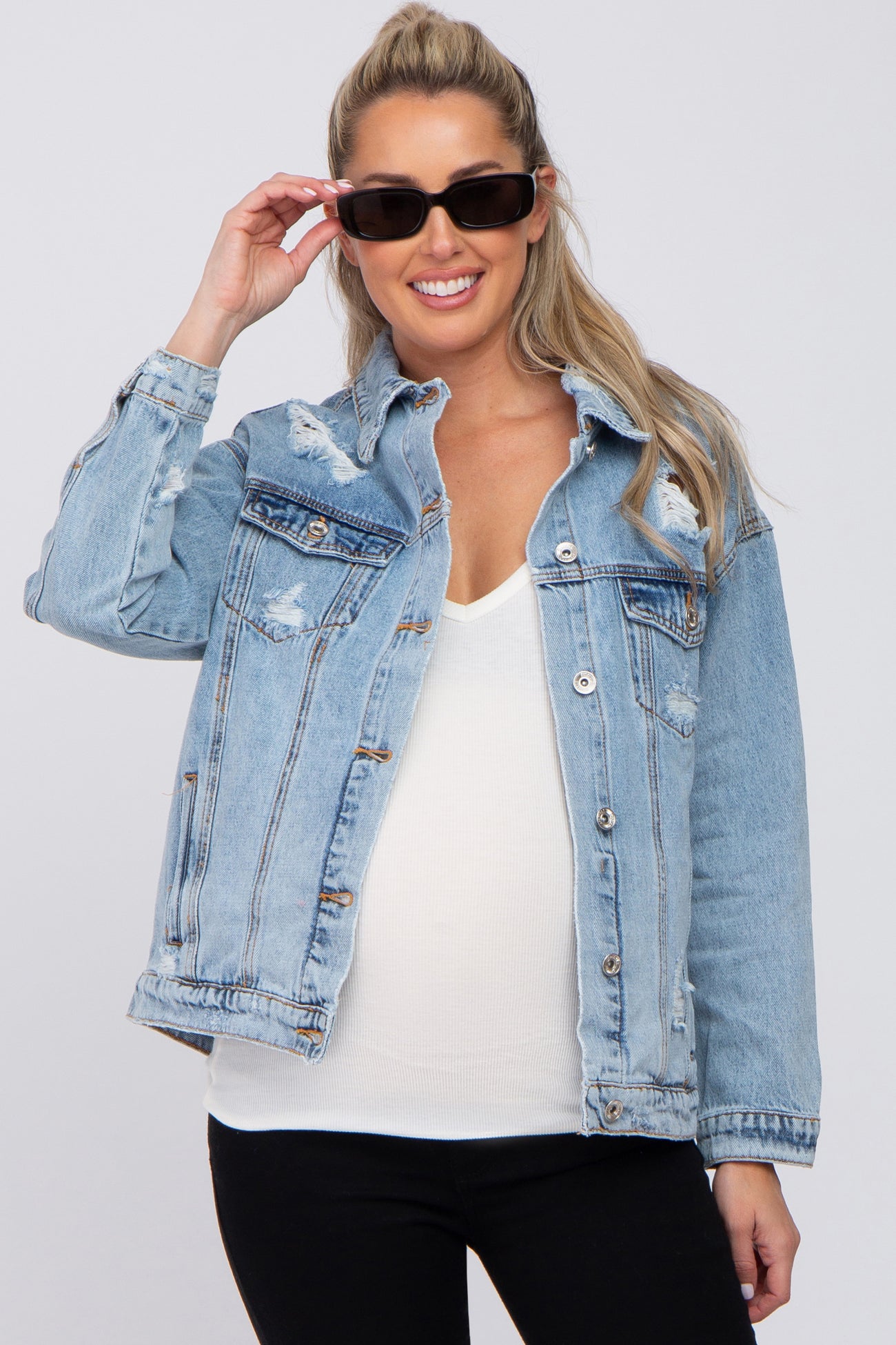 smiling woman wearing a distressed light wash denim jacket and black sunglasses over a white top