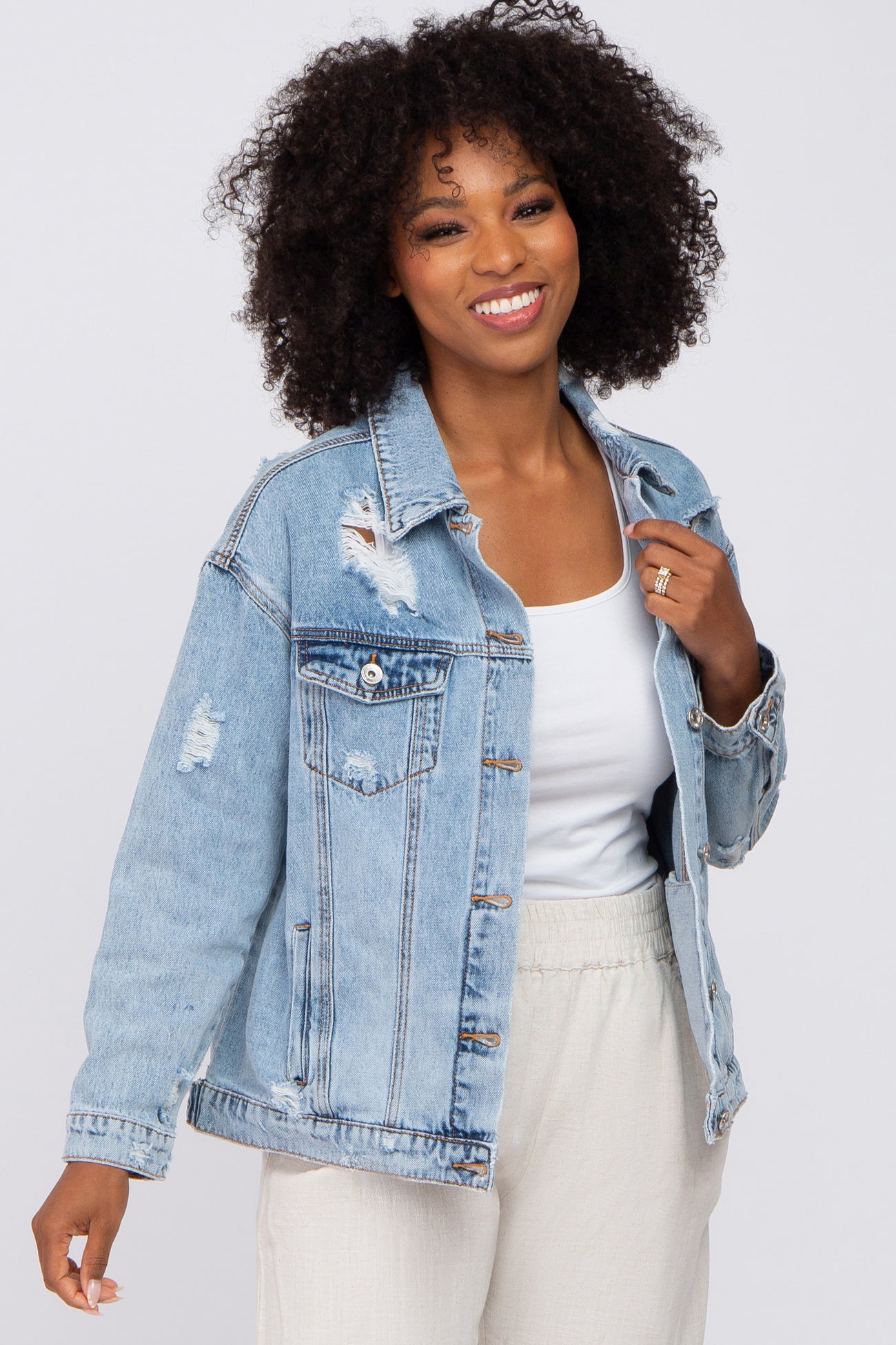smiling woman with curly hair wearing a distressed light wash denim jacket over a white top
