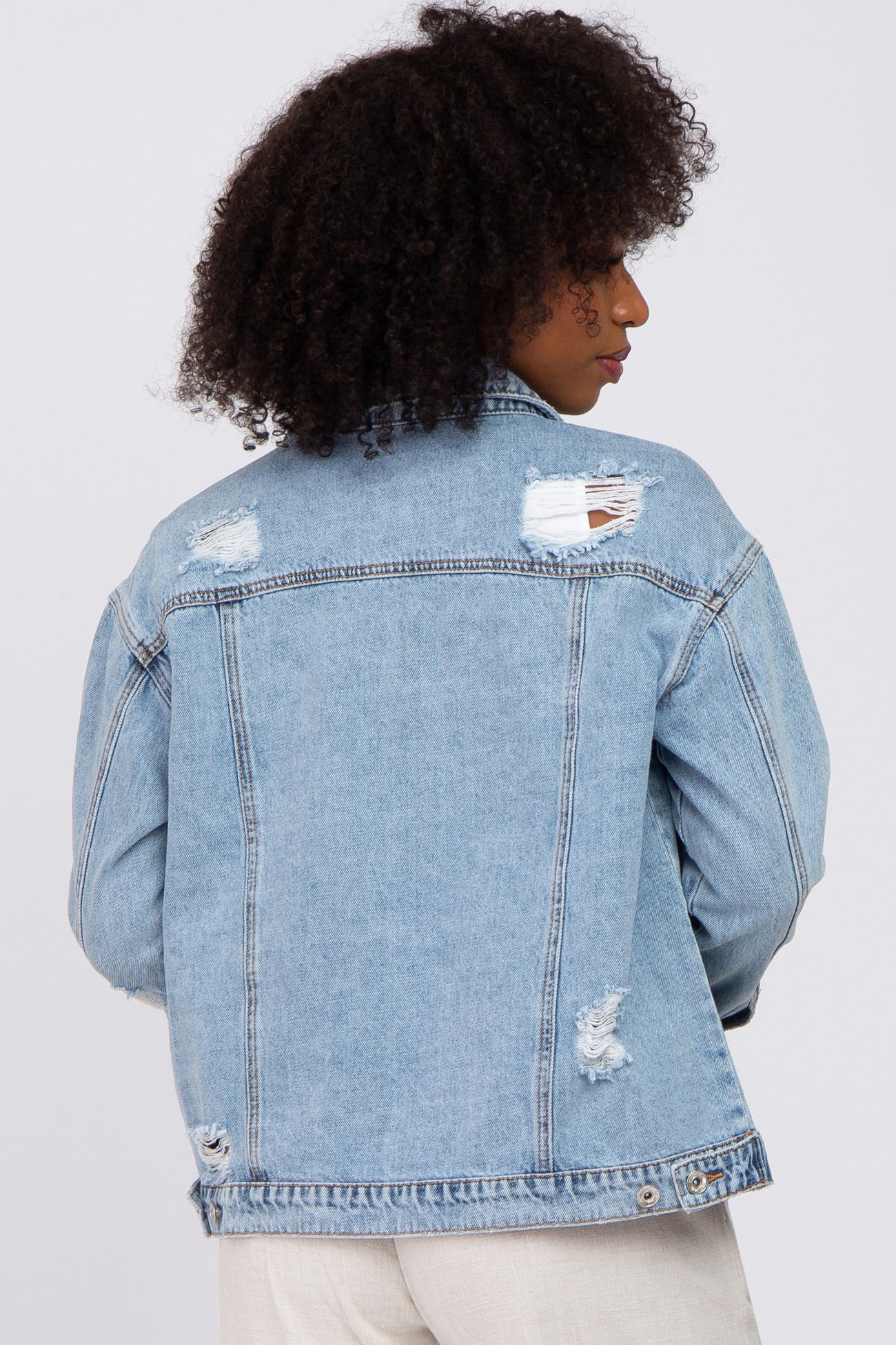 Back view of a woman wearing a light wash distressed denim jacket with ripped details and frayed edges