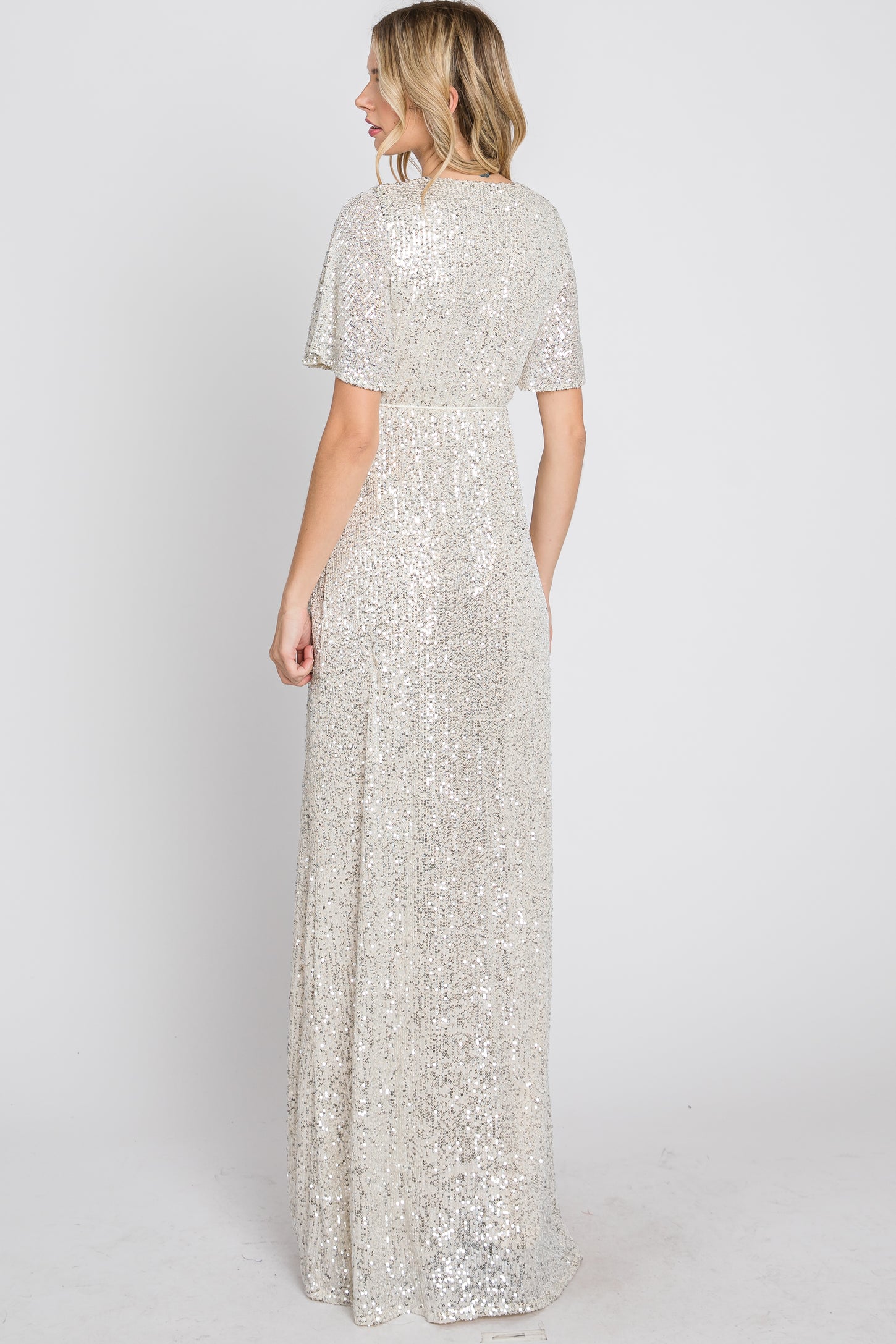 woman wearing a silver sequin evening gown with short flutter sleeves and a flowing skirt, viewed from the back