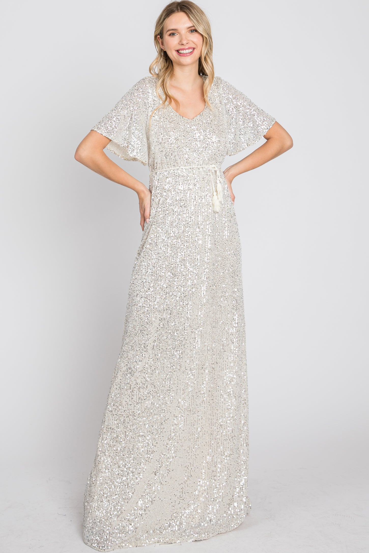 woman wearing a floor-length silver sequin gown with flutter sleeves and a tie waist detail