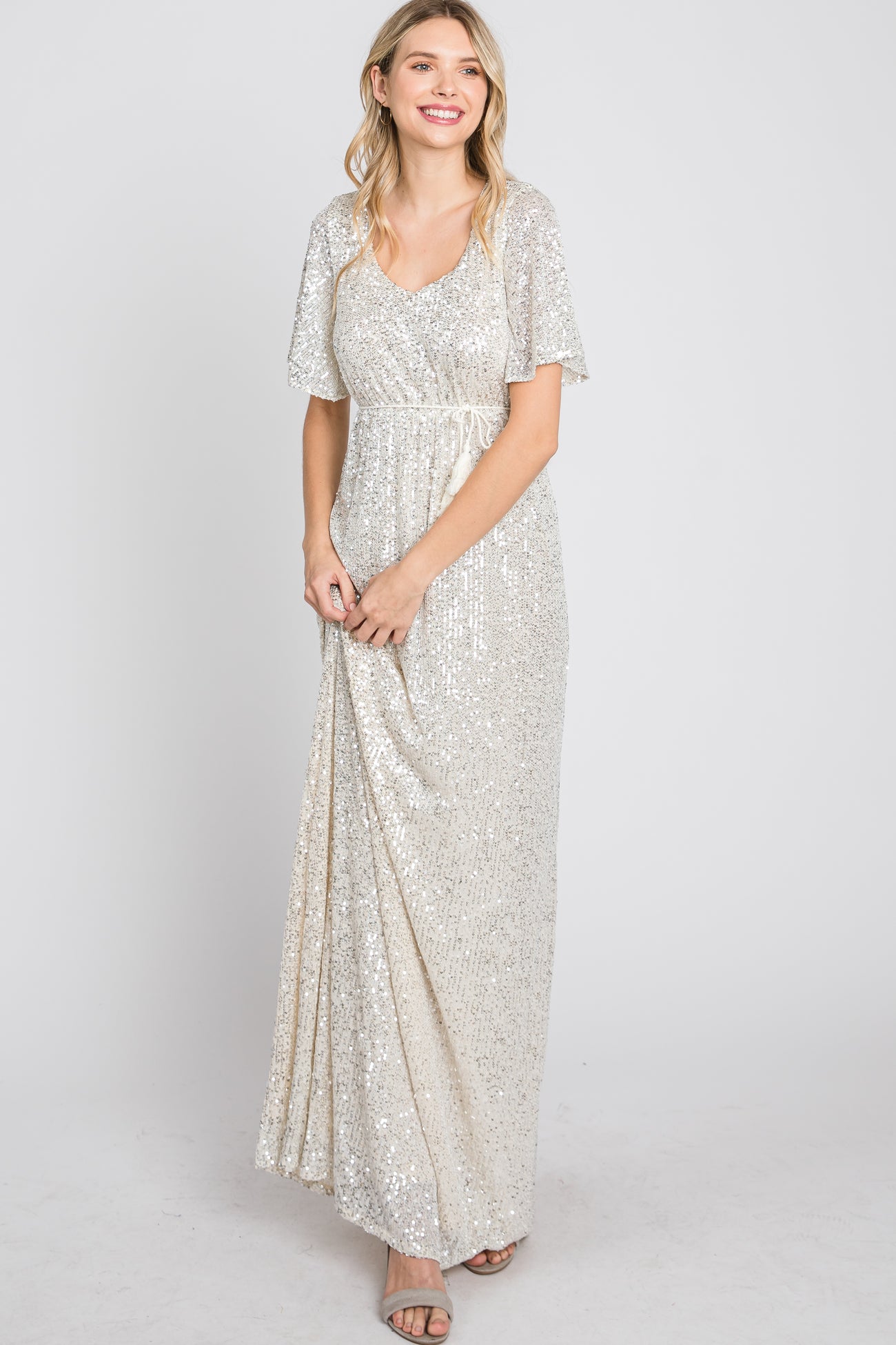woman wearing a shimmering silver sequin maxi dress with short flutter sleeves and a fitted waist