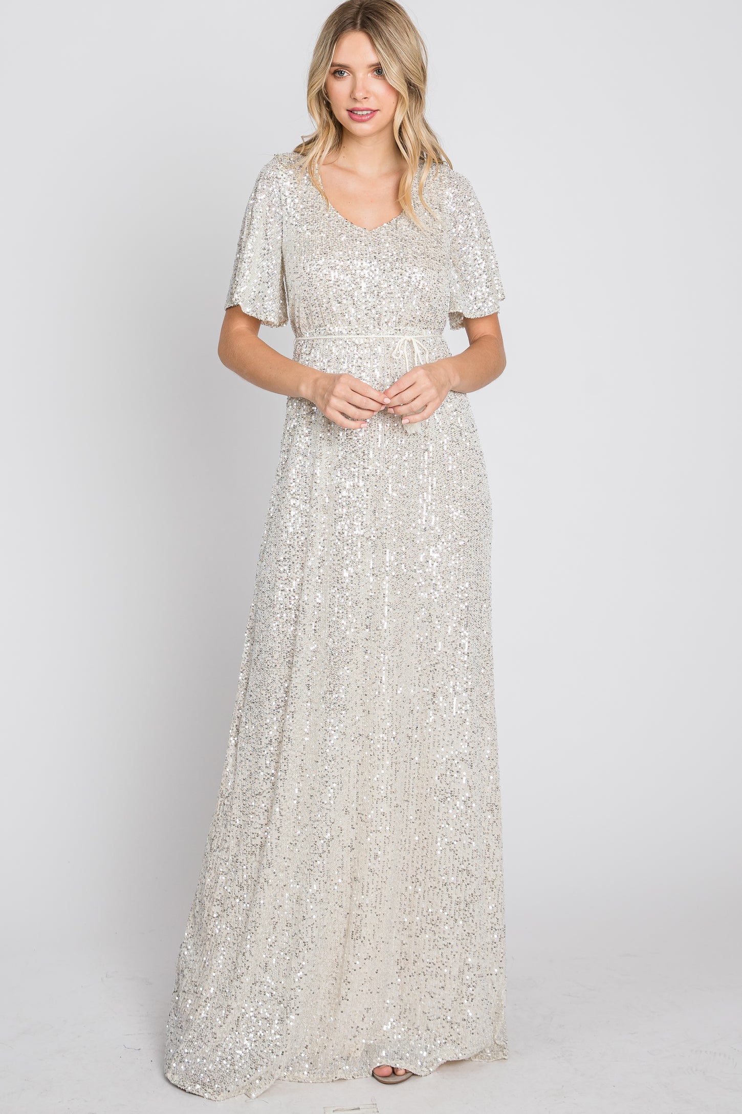 woman wearing a silver sequin maxi dress with flutter sleeves and a fitted waist