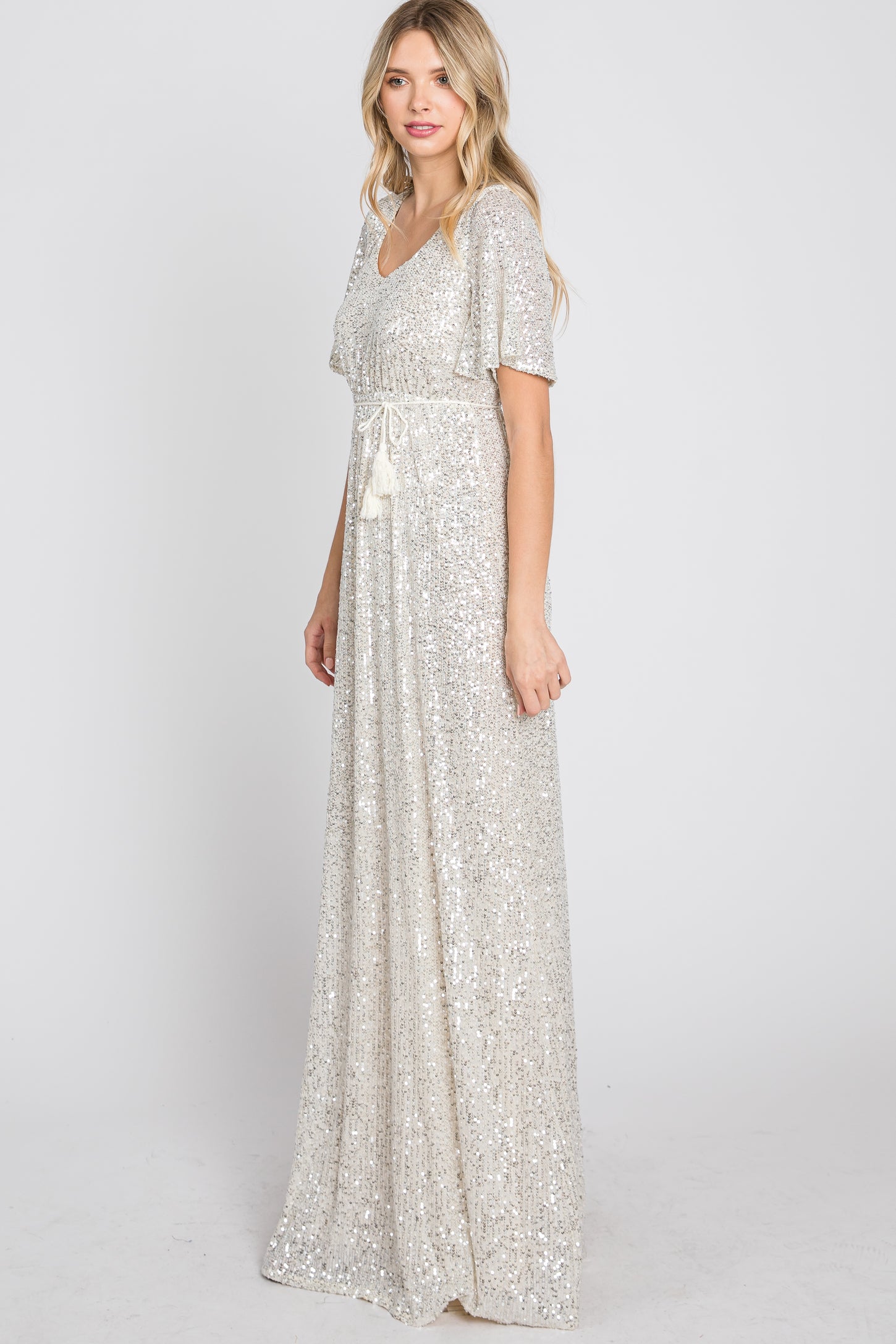 woman wearing a shimmering silver sequin maxi dress with a v-neckline and short flutter sleeves