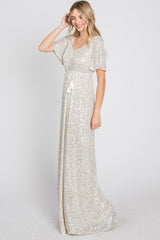Woman wearing a white sequin maxi dress with flutter sleeves and a tassel waist tie