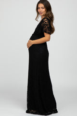 Pregnant woman in a black lace maternity maxi dress with short sleeves posing against a white background