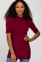 woman with curly hair wearing a burgundy short sleeve mock neck top and blue jeans