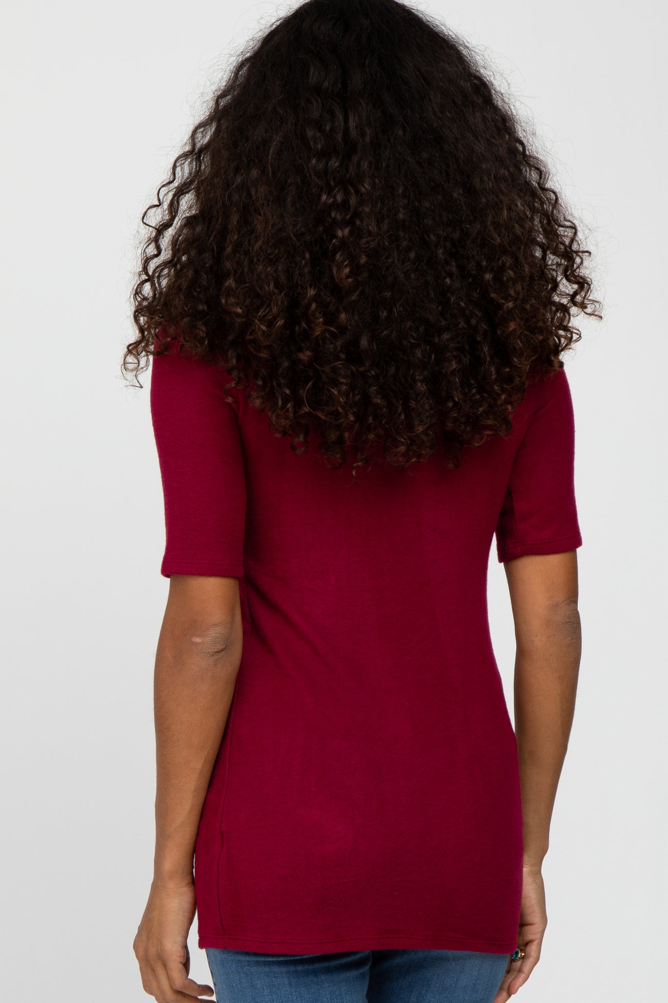 back view of a woman with long curly dark hair wearing a maroon short sleeve t-shirt and blue jeans