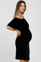 Pregnant woman wearing a black velvet off-the-shoulder maternity dress with ruffle detail