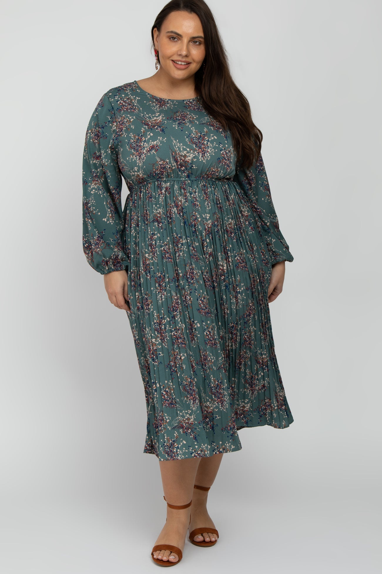 Plus size woman wearing a long sleeve teal floral pleated midi dress with brown sandals