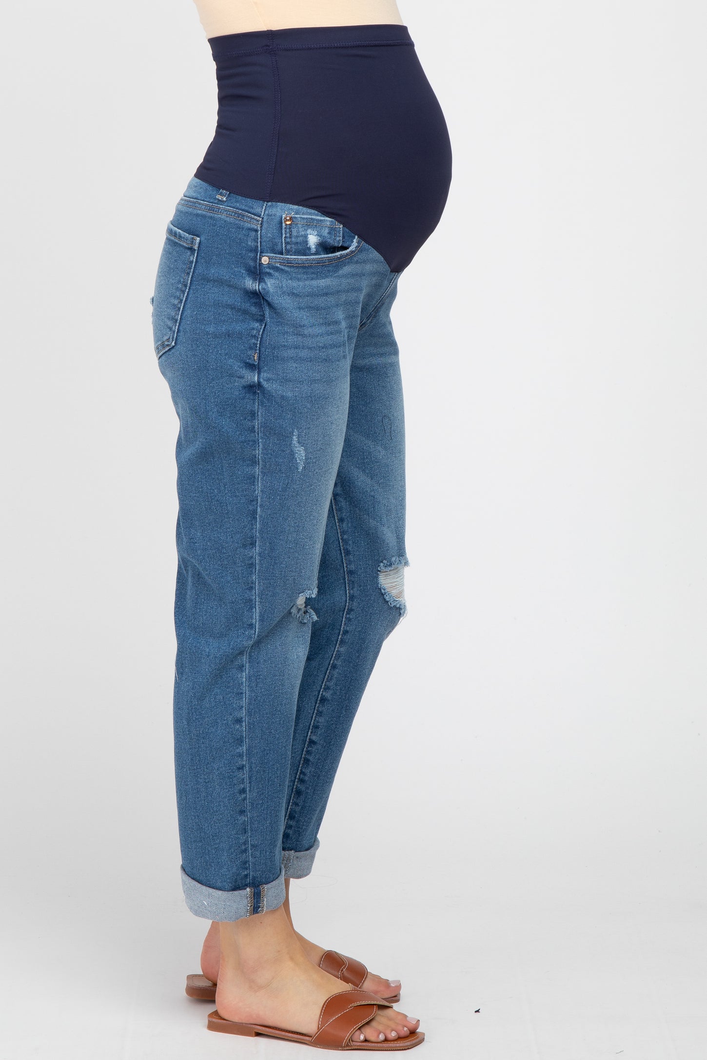 pregnant woman wearing distressed maternity boyfriend jeans with a navy blue belly band and brown sandals