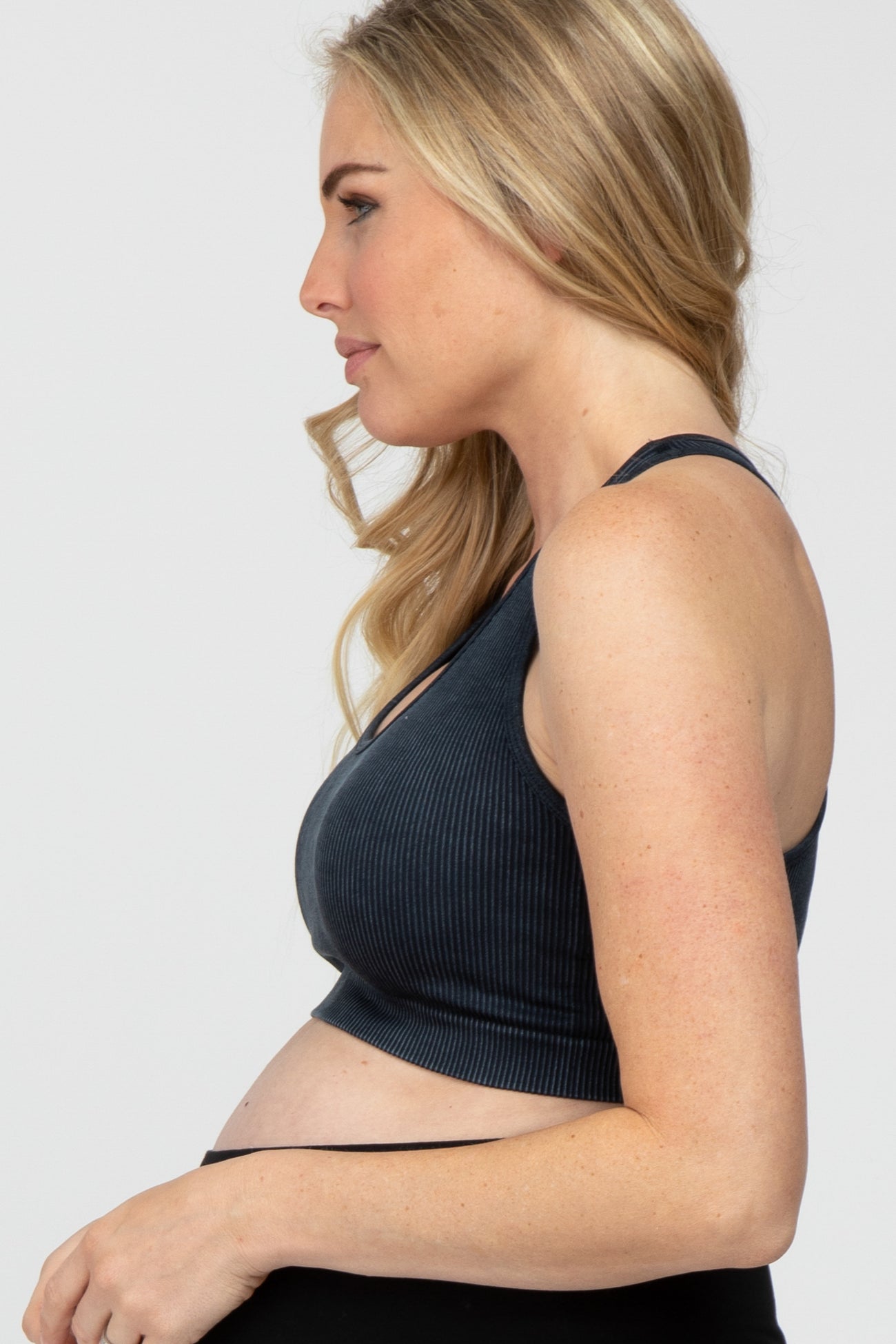 Side profile of a pregnant woman wearing a black ribbed maternity sports bra and leggings against a white background