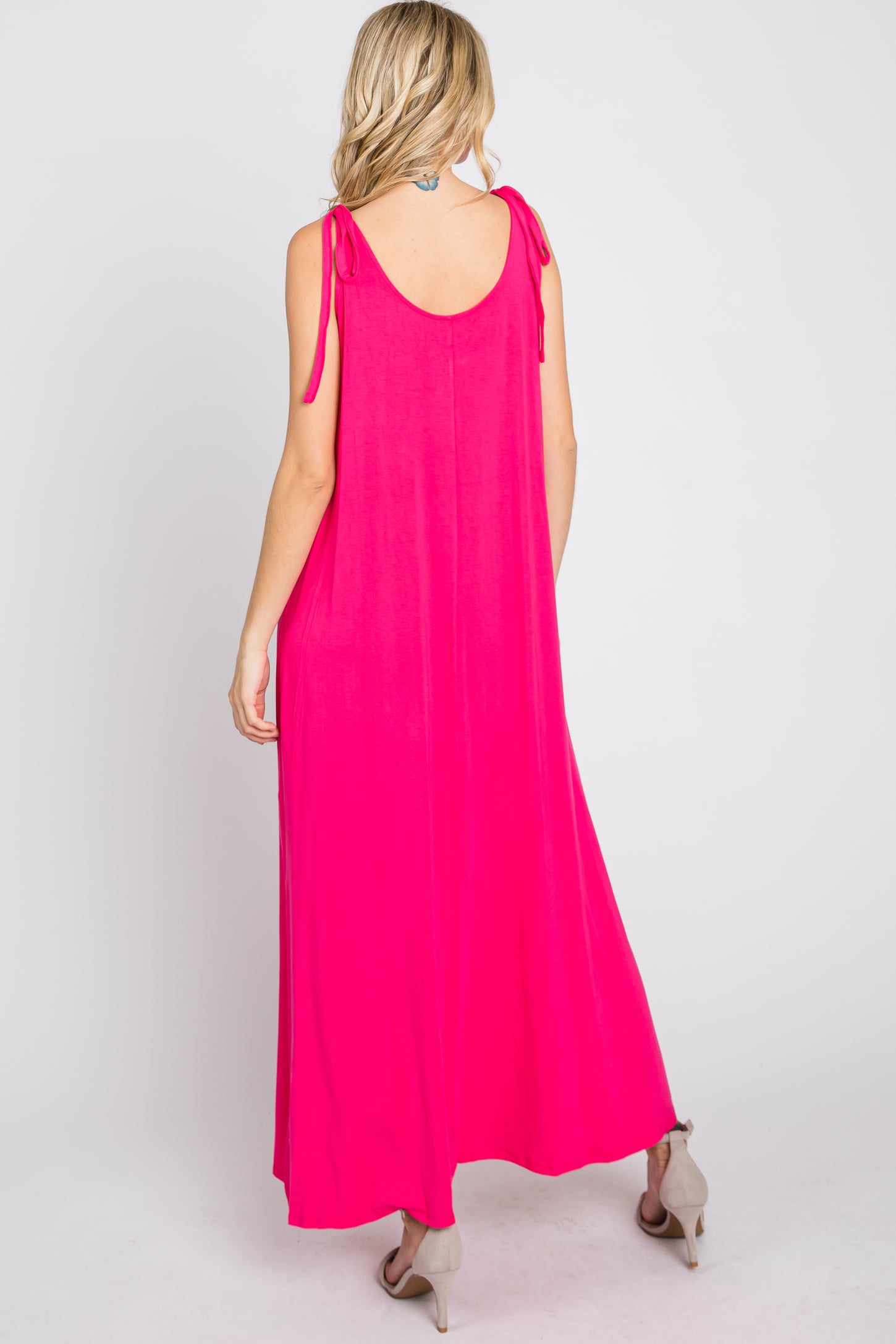 woman from behind wearing a hot pink sleeveless maxi dress with tie-shoulder straps and tan heels