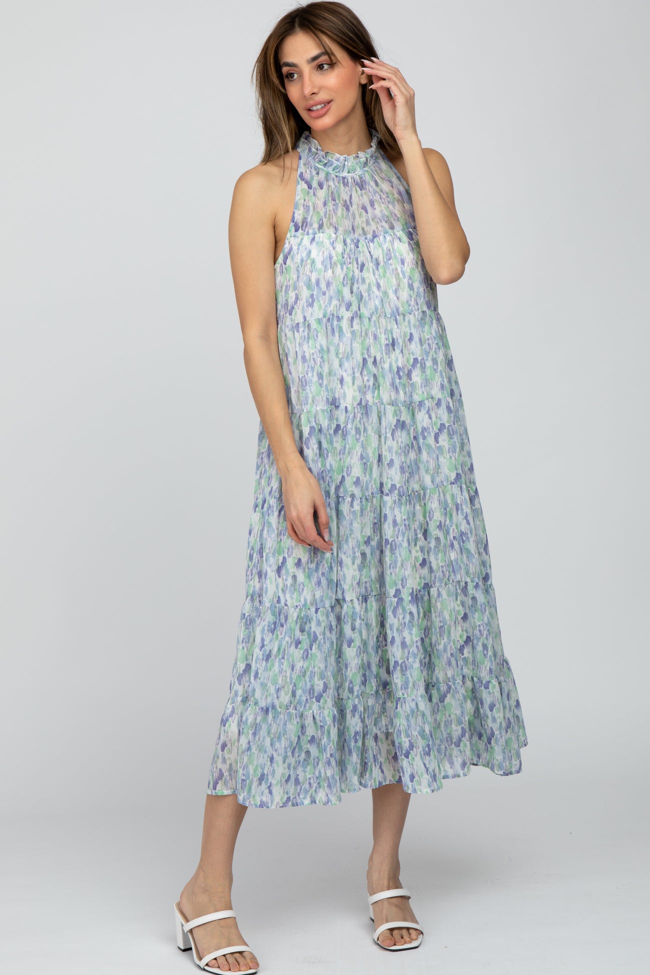 woman wearing a sleeveless floral midi dress in light blue and green with a flowing silhouette and a halter neck design