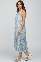 woman wearing a flowy sleeveless midi dress with a floral pattern in green and purple, paired with white block heel sandals