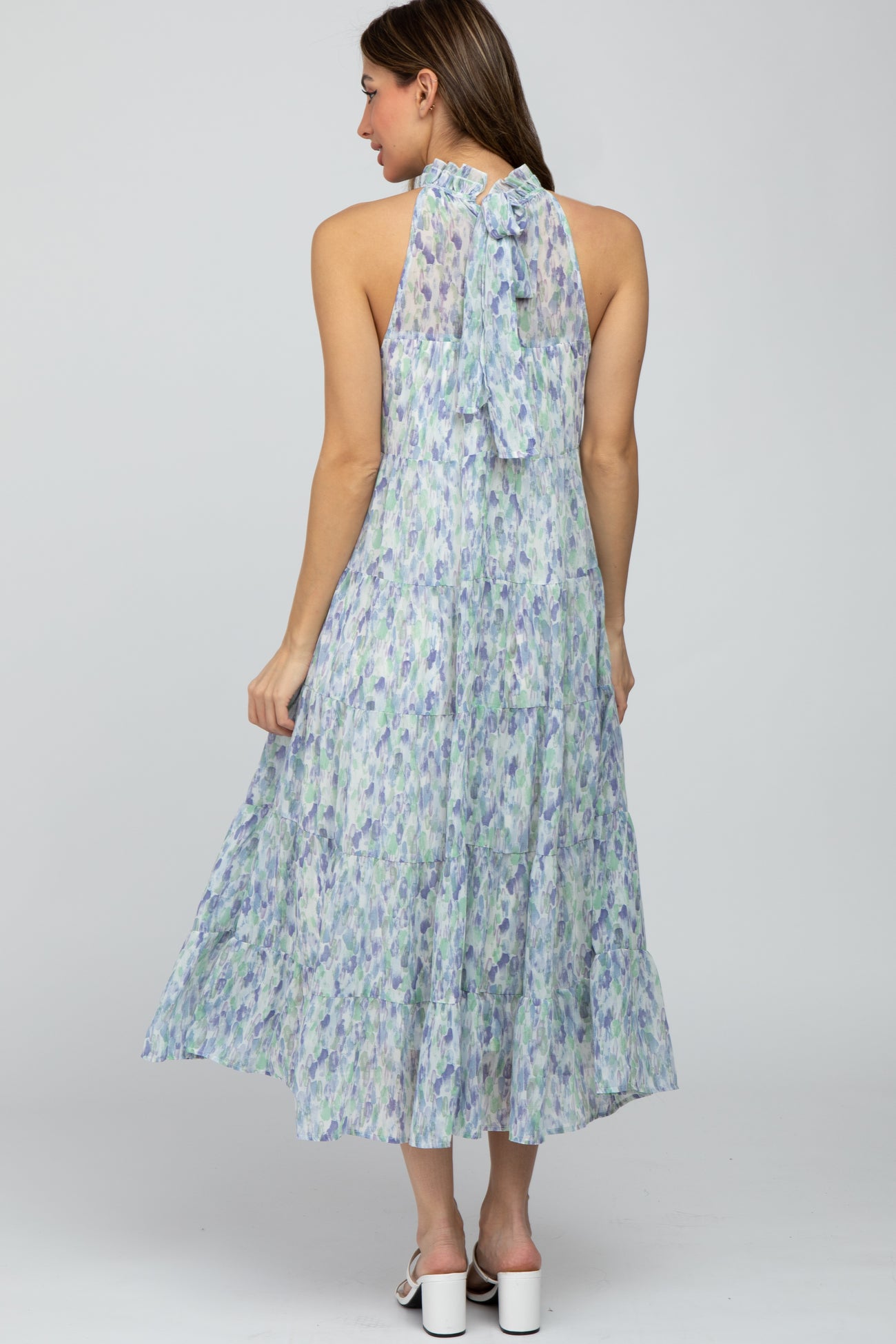 Woman wearing a tiered halter midi dress with a blue and purple watercolor print and a tie-neck back.
