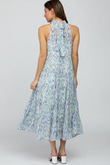 Woman wearing a tiered halter midi dress with a blue and purple watercolor print and a tie-neck back.