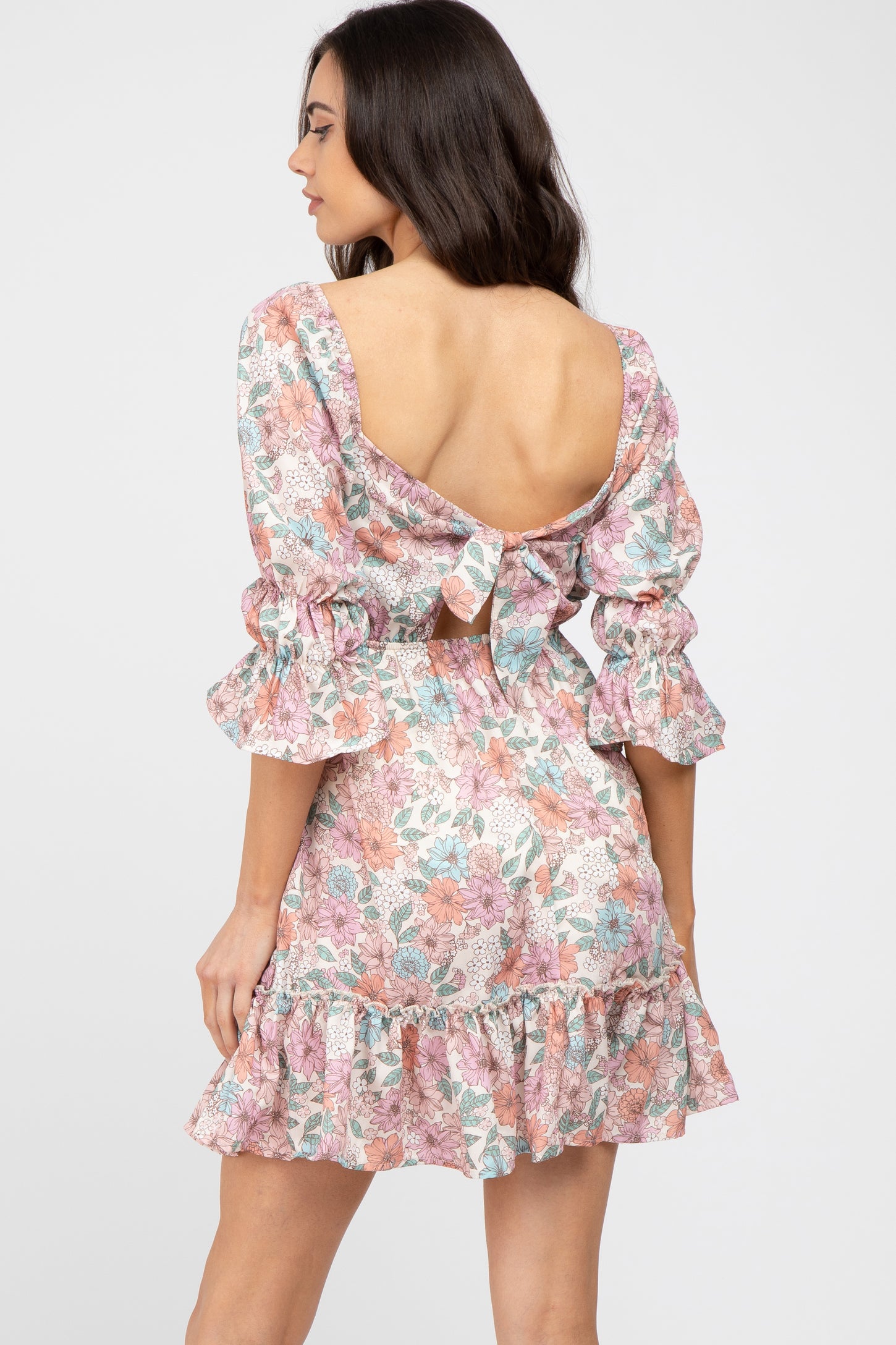 Woman wearing a floral mini dress with a tie-back cutout and ruffled sleeves against a white background