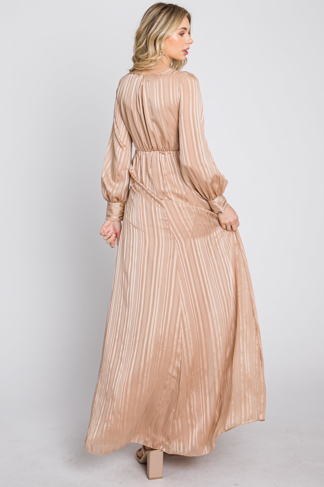 woman wearing a long beige striped maxi dress with balloon sleeves and open back, shown from the back