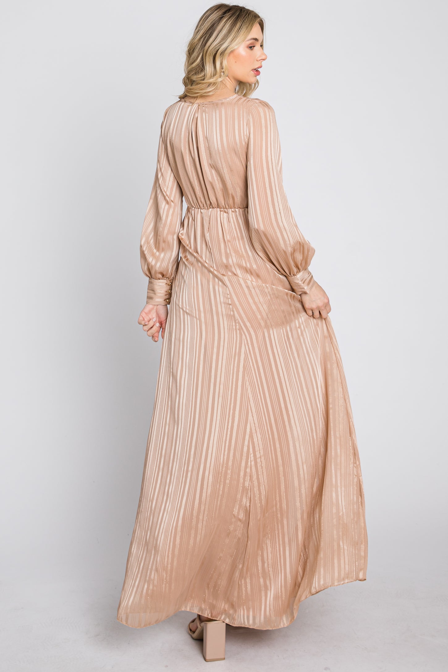 woman wearing a long beige striped maxi dress with balloon sleeves and open back, shown from the back