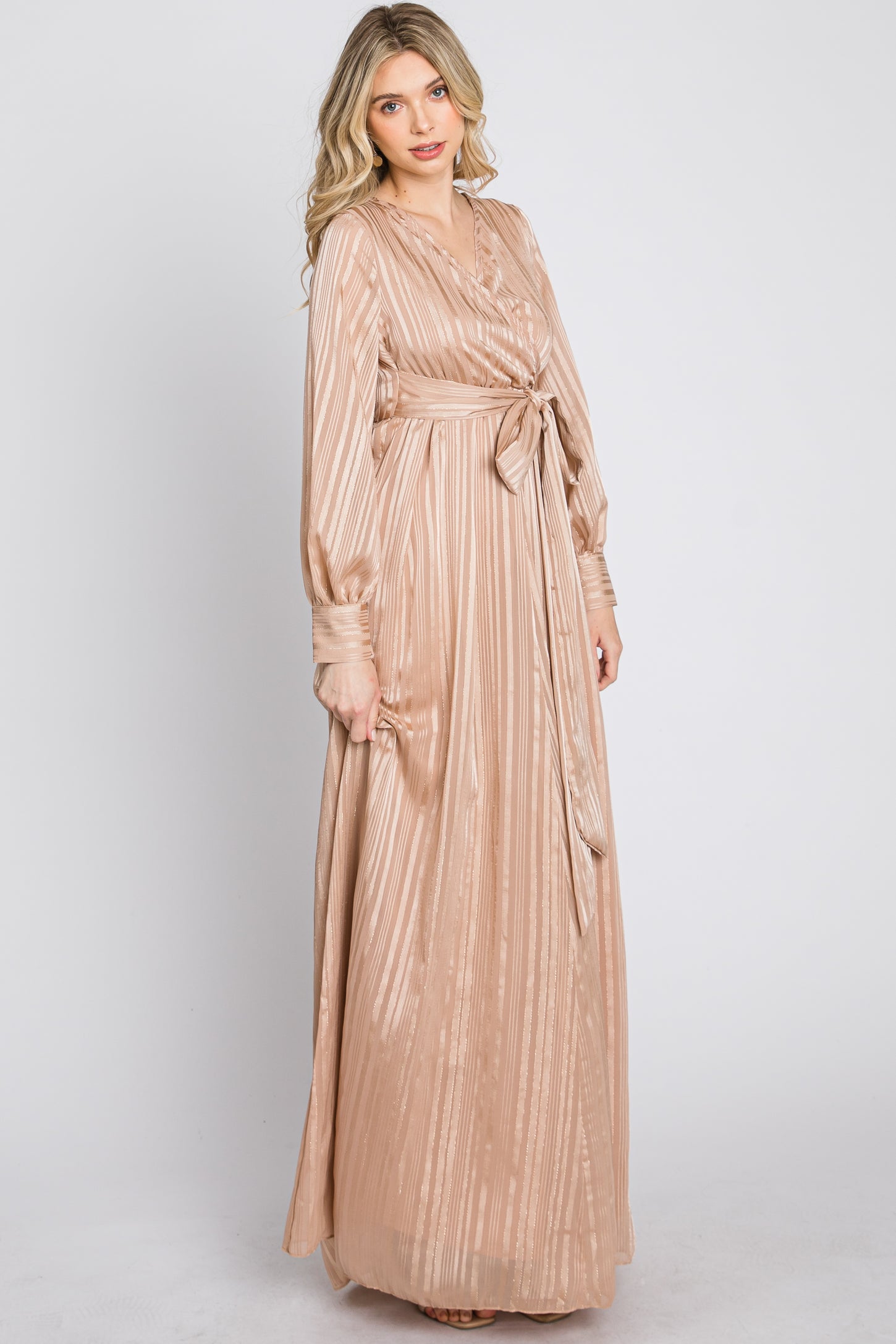 woman wearing a long beige striped maxi dress with long sleeves and a tie waist detail