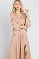 woman wearing a champagne-colored long sleeve wrap dress with pleated details and a tied waist