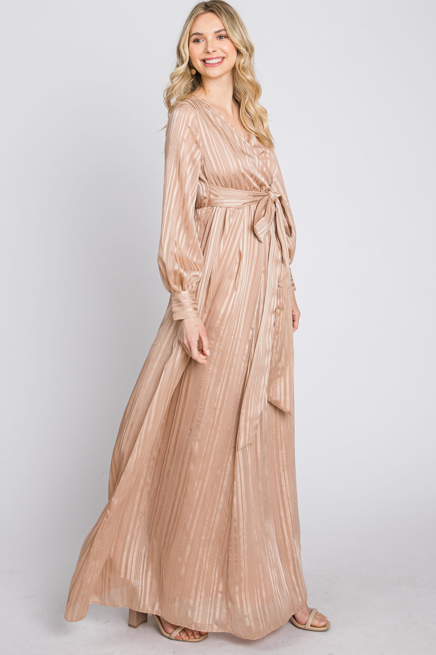 woman wearing a blush long sleeve pleated maxi dress with a tie waist detail and a flowing silhouette