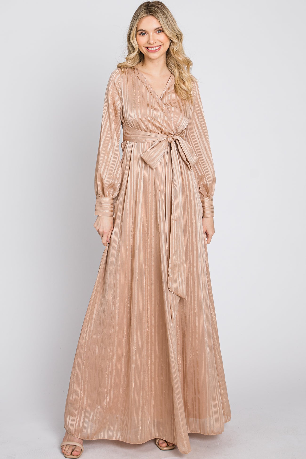 woman wearing a long champagne-colored maxi dress with a belted waist and long sleeves