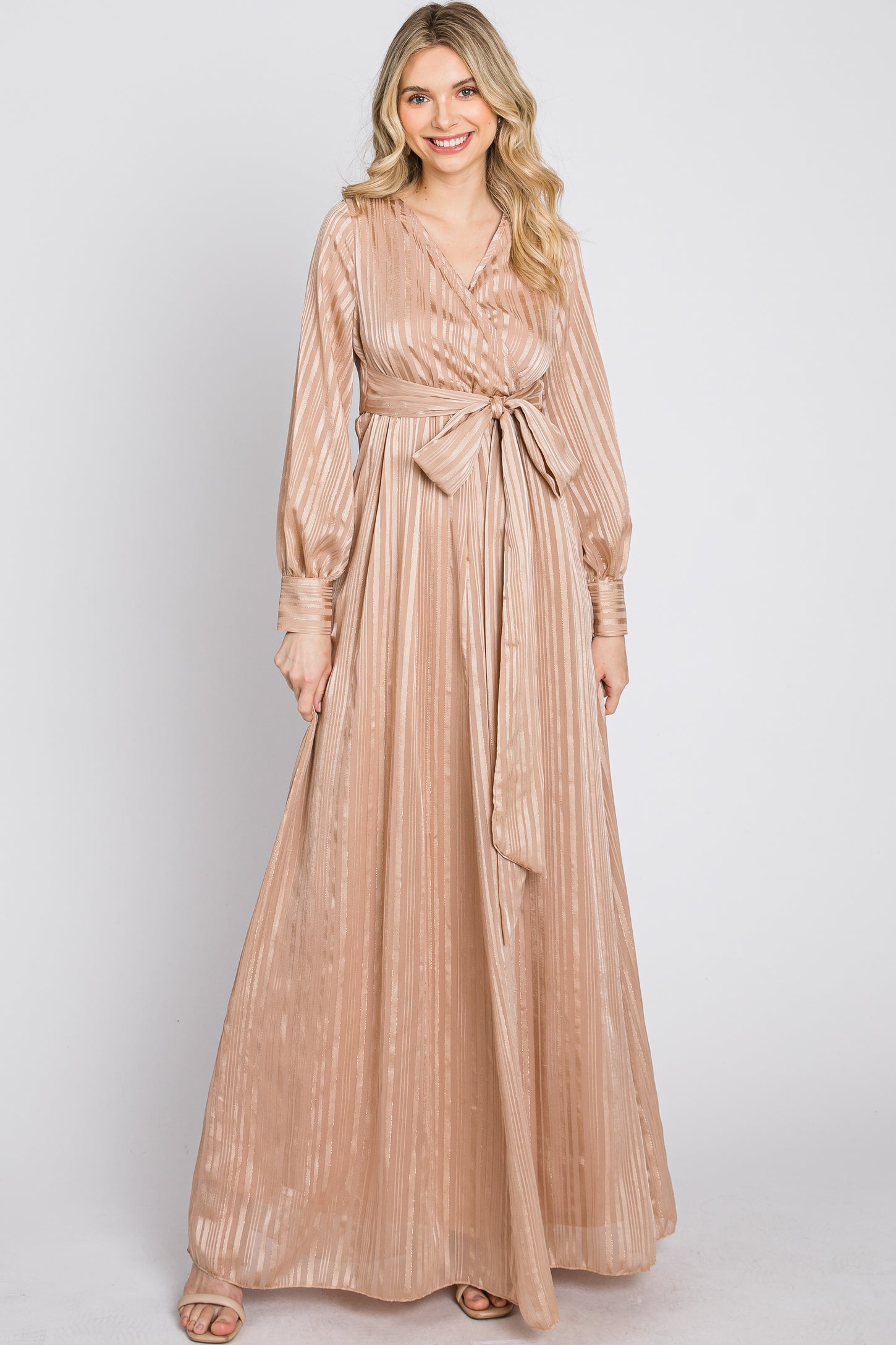 woman wearing a long champagne-colored maxi dress with a belted waist and long sleeves