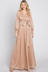 woman wearing a long champagne-colored maxi dress with a belted waist and long sleeves