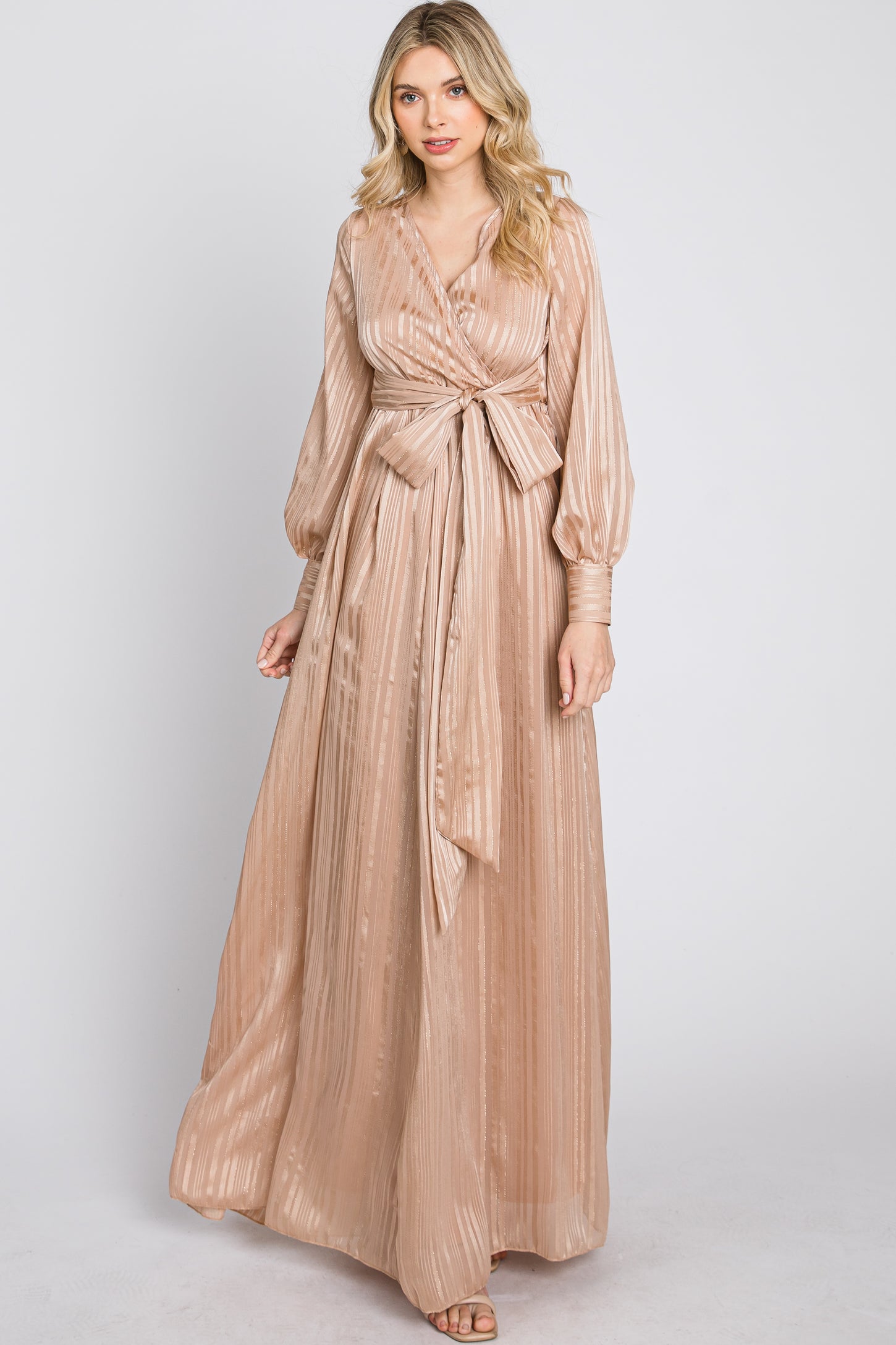 woman wearing a long sleeve champagne colored maxi dress with a tie waist and vertical ribbed texture