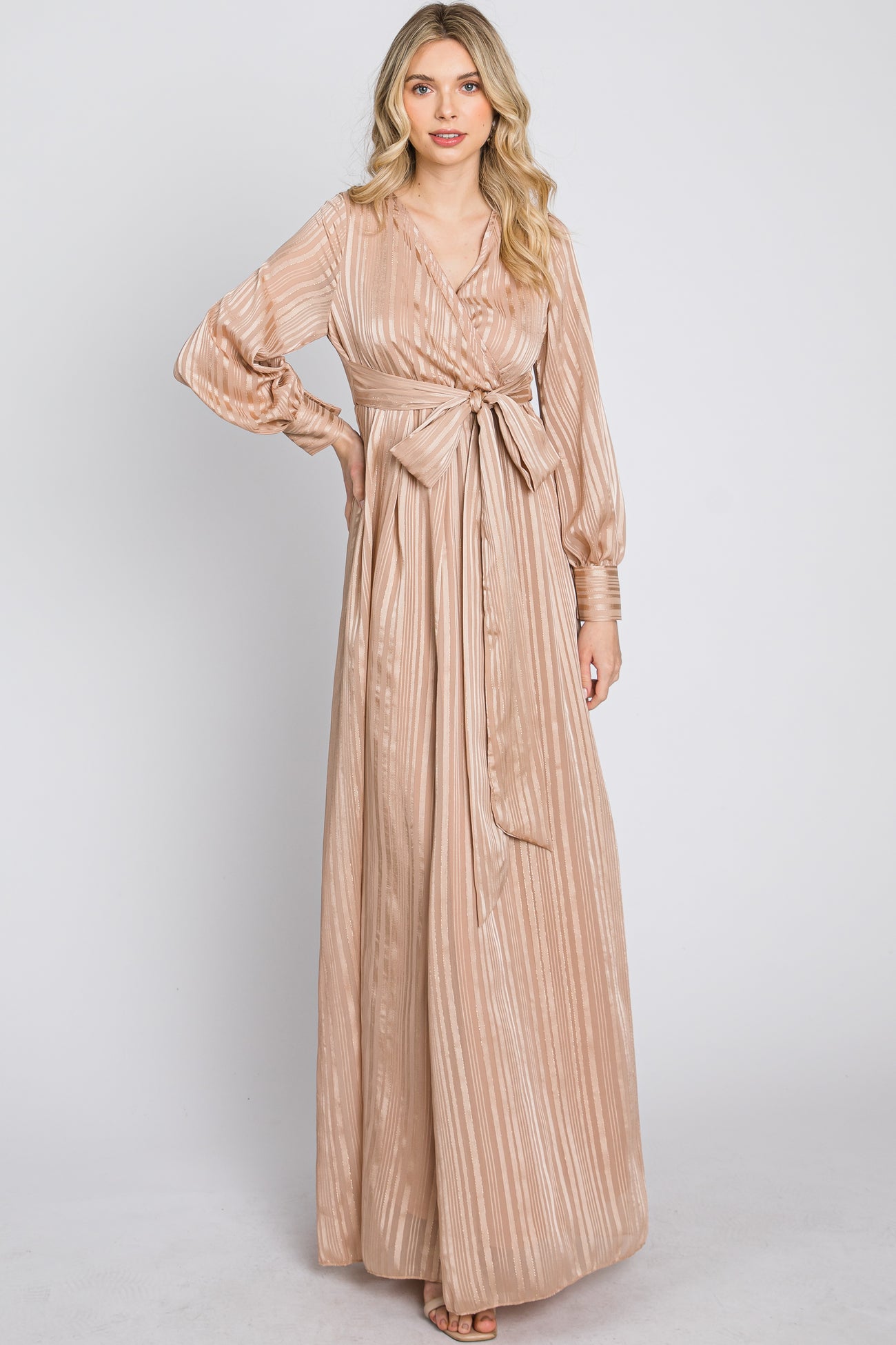 woman wearing a champagne-colored striped maxi dress with a tie waist and long sleeves