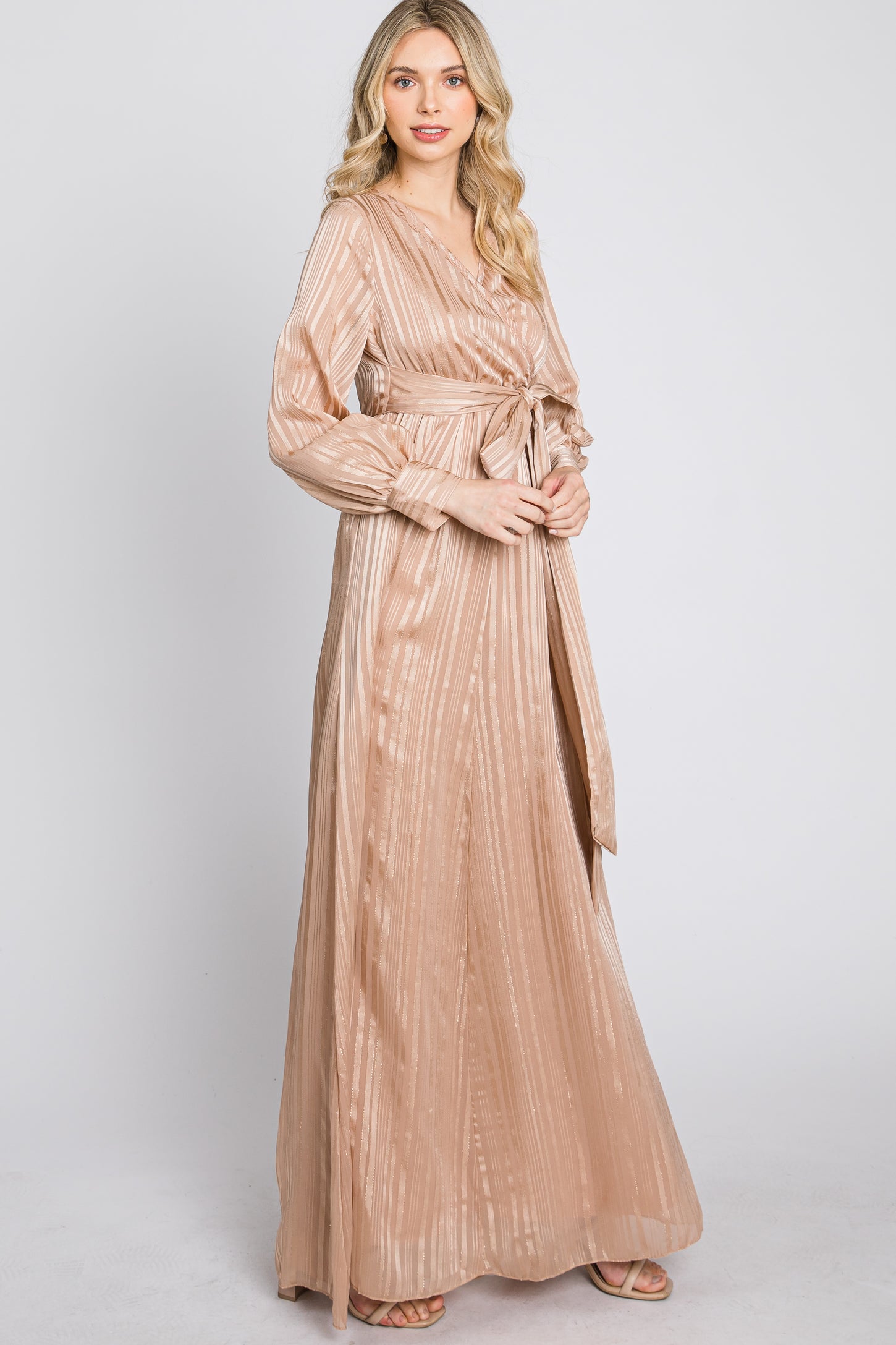 woman wearing a long champagne-colored maxi dress with a tie waist and long sleeves