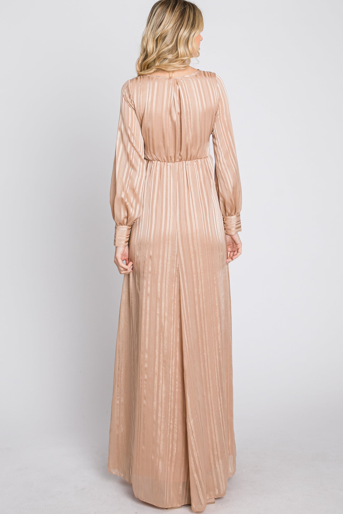 woman wearing a long, light beige pleated dress with long sleeves and a cinched waist, shown from the back