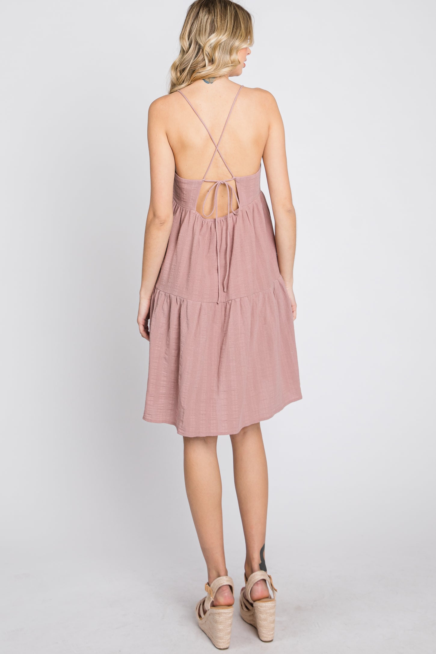 Back view of a woman wearing a mauve tiered mini dress with crisscross spaghetti straps and wedge sandals