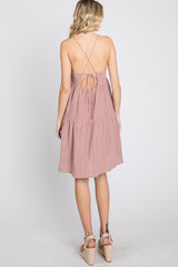 Back view of a woman wearing a mauve tiered mini dress with crisscross spaghetti straps and wedge sandals