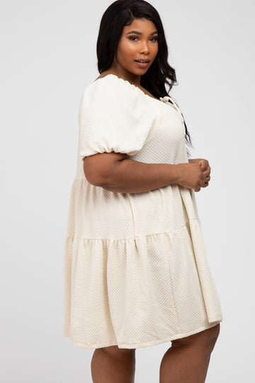 woman wearing a cream colored plus size puff sleeve tiered mini dress with textured fabric