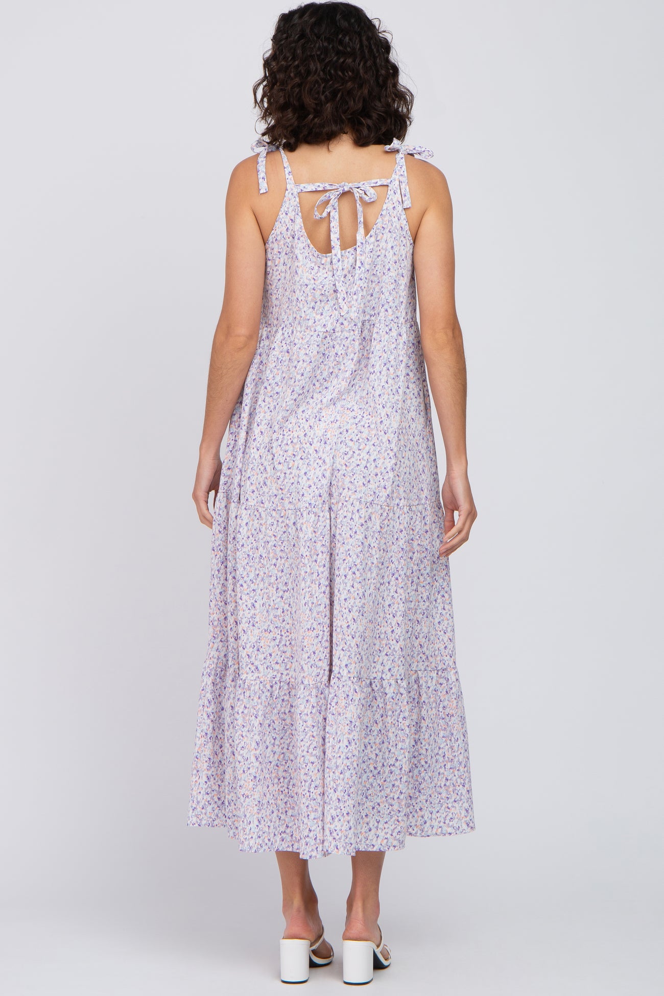 Back view of a woman wearing a purple floral tiered maxi dress with tie straps and a bow detail.