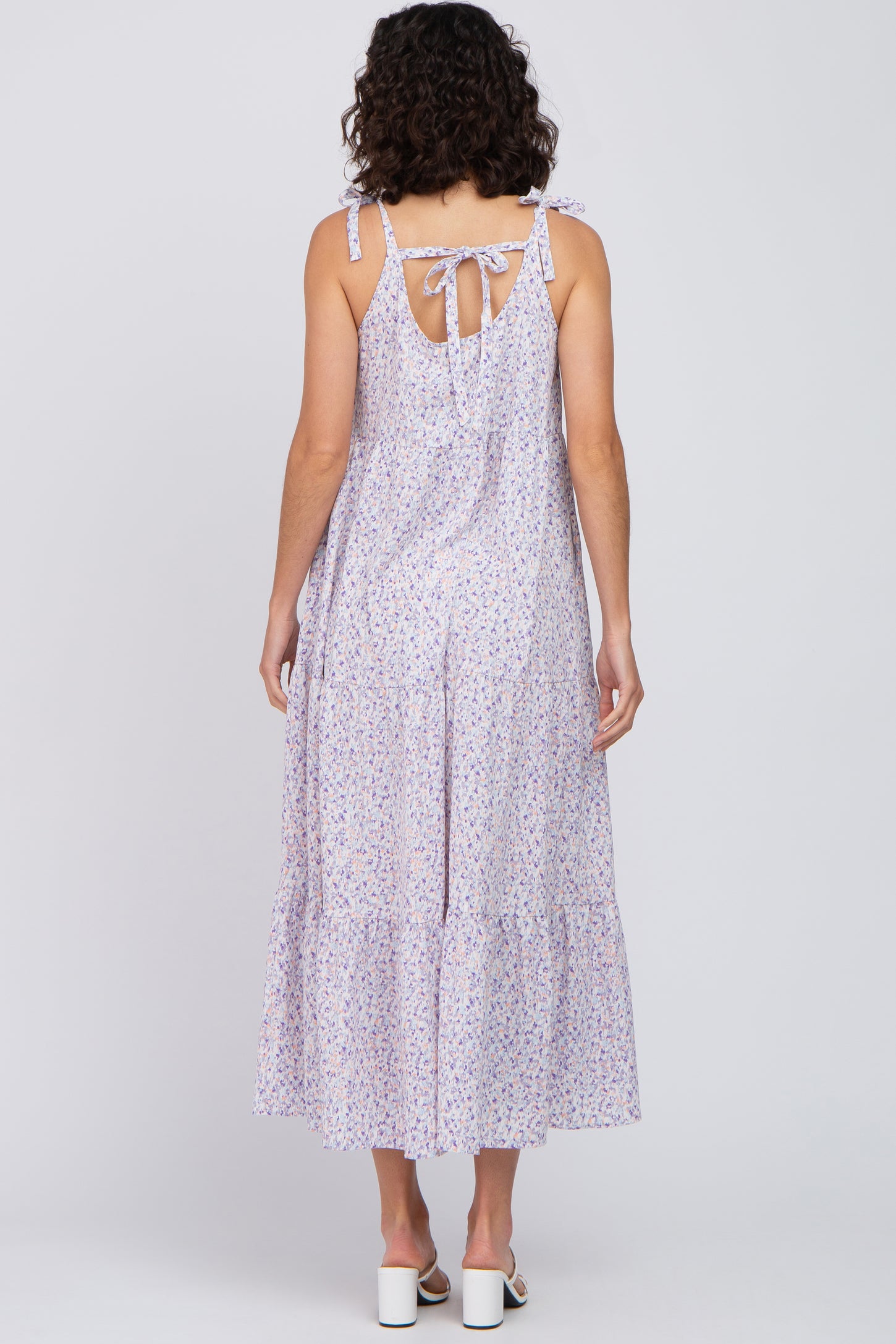 Back view of a woman wearing a purple floral tiered maxi dress with tie straps and a bow detail.