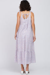 Back view of a woman wearing a purple floral tiered maxi dress with tie straps and a bow detail.