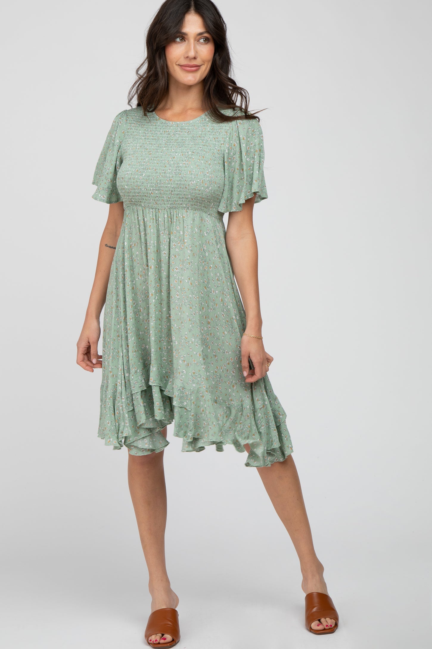 woman wearing a sage green floral smocked maternity dress with ruffle hem and brown slide sandals