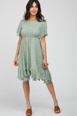 woman wearing a sage green floral smocked maternity dress with ruffle hem and brown slide sandals