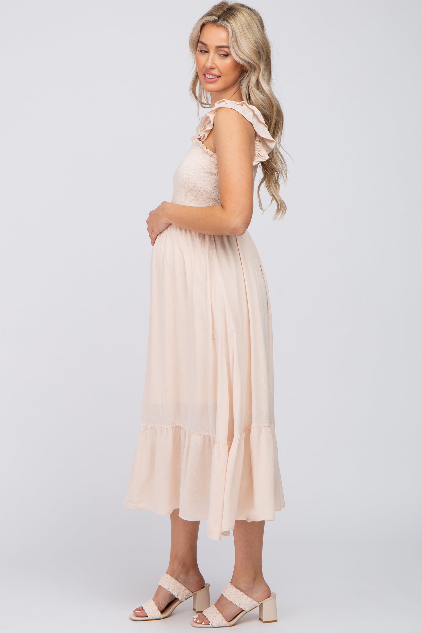 pregnant woman in cream smocked maternity midi dress with ruffle sleeves and block heel sandals