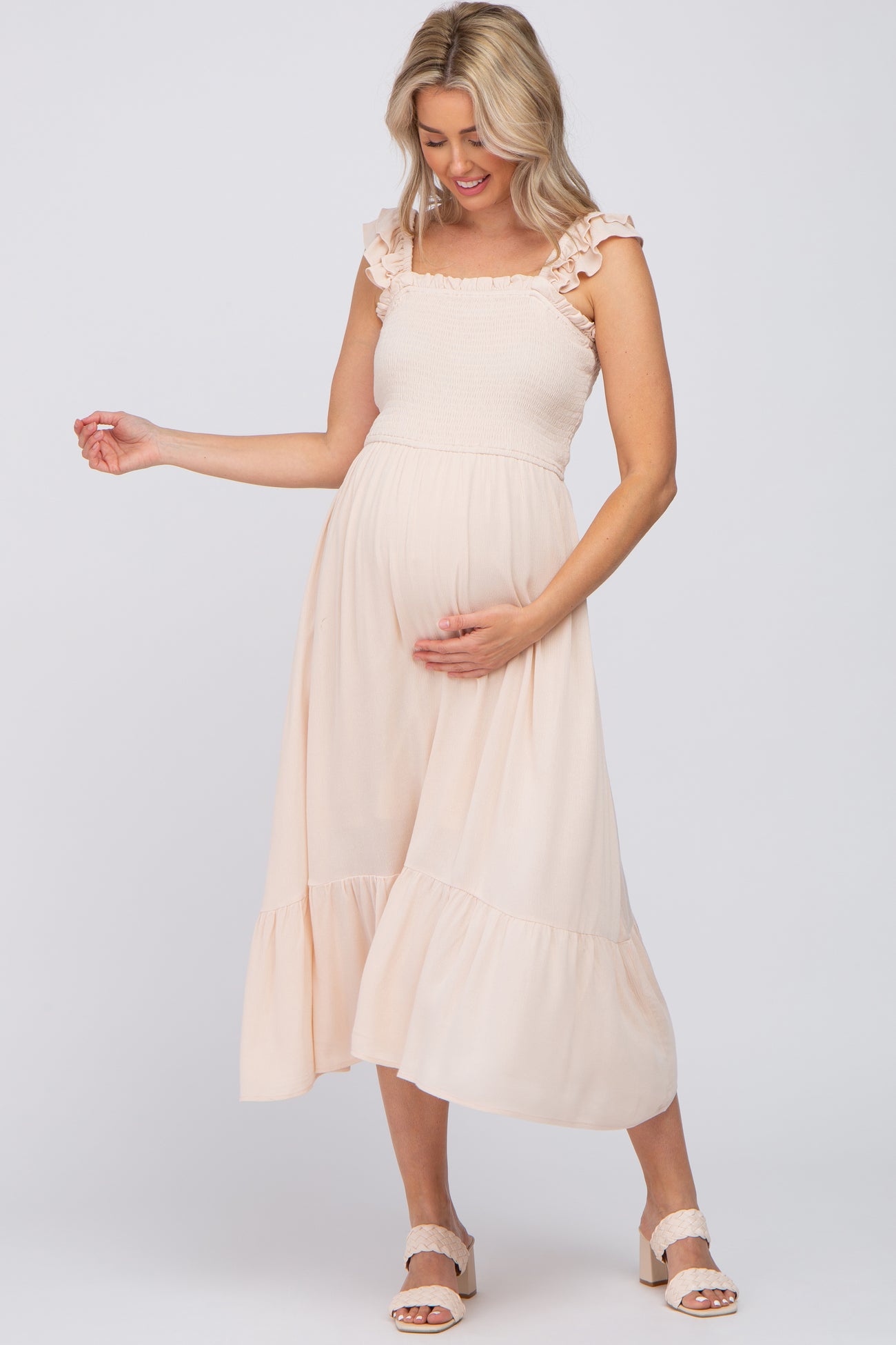 Pregnant woman in a light pink smocked maternity midi dress with ruffle straps and tiered skirt