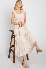 woman in cream smocked midi dress with ruffle straps sitting on a bamboo stool holding a straw handbag